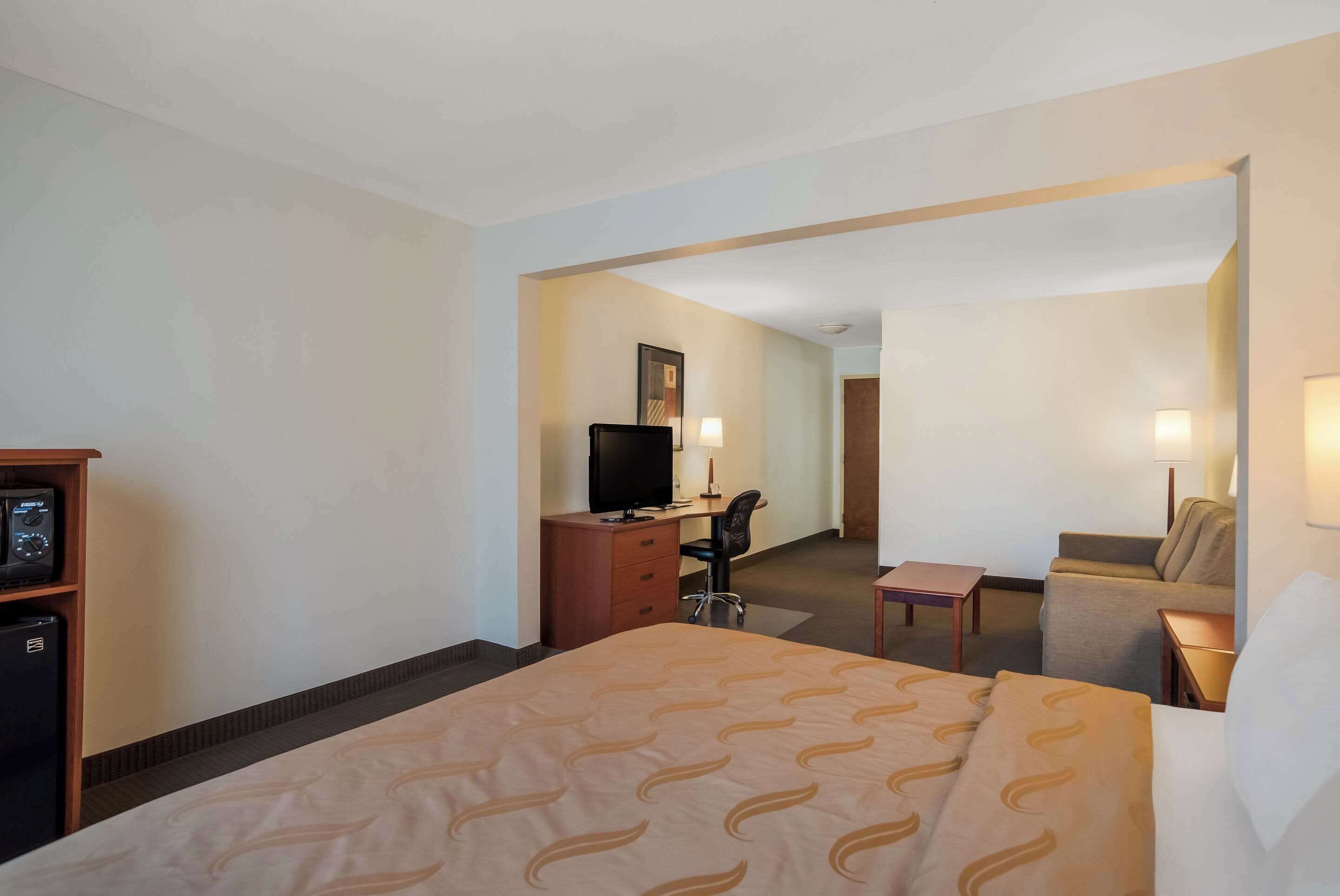 A hotel room with a bed, a desk with a computer, a television, and a small table.