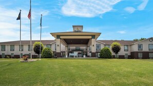 A hotel with a central entrance, multiple flags, and a well-maintained lawn. - Quality Inn & Suites Chambersburg Northeast (Chambersburg)