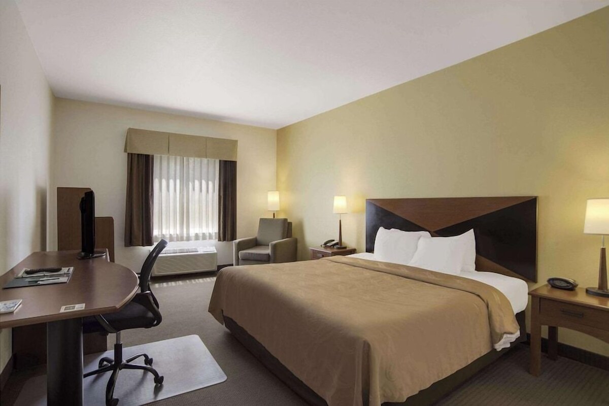 Ein Hotelzimmer mit Bett, Schreibtisch, Stuhl und zwei Nachttischen mit Lampen.