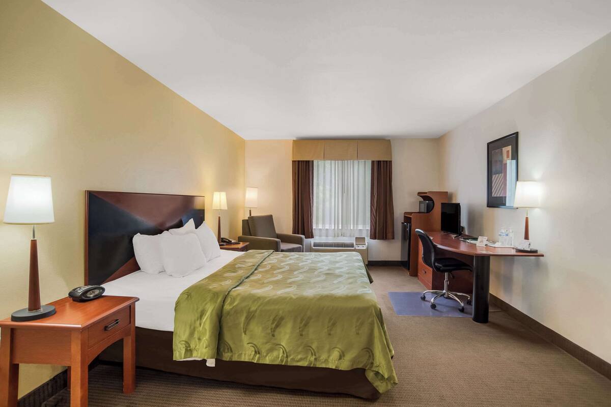 A hotel room with a large bed, a desk, a chair, and a TV.