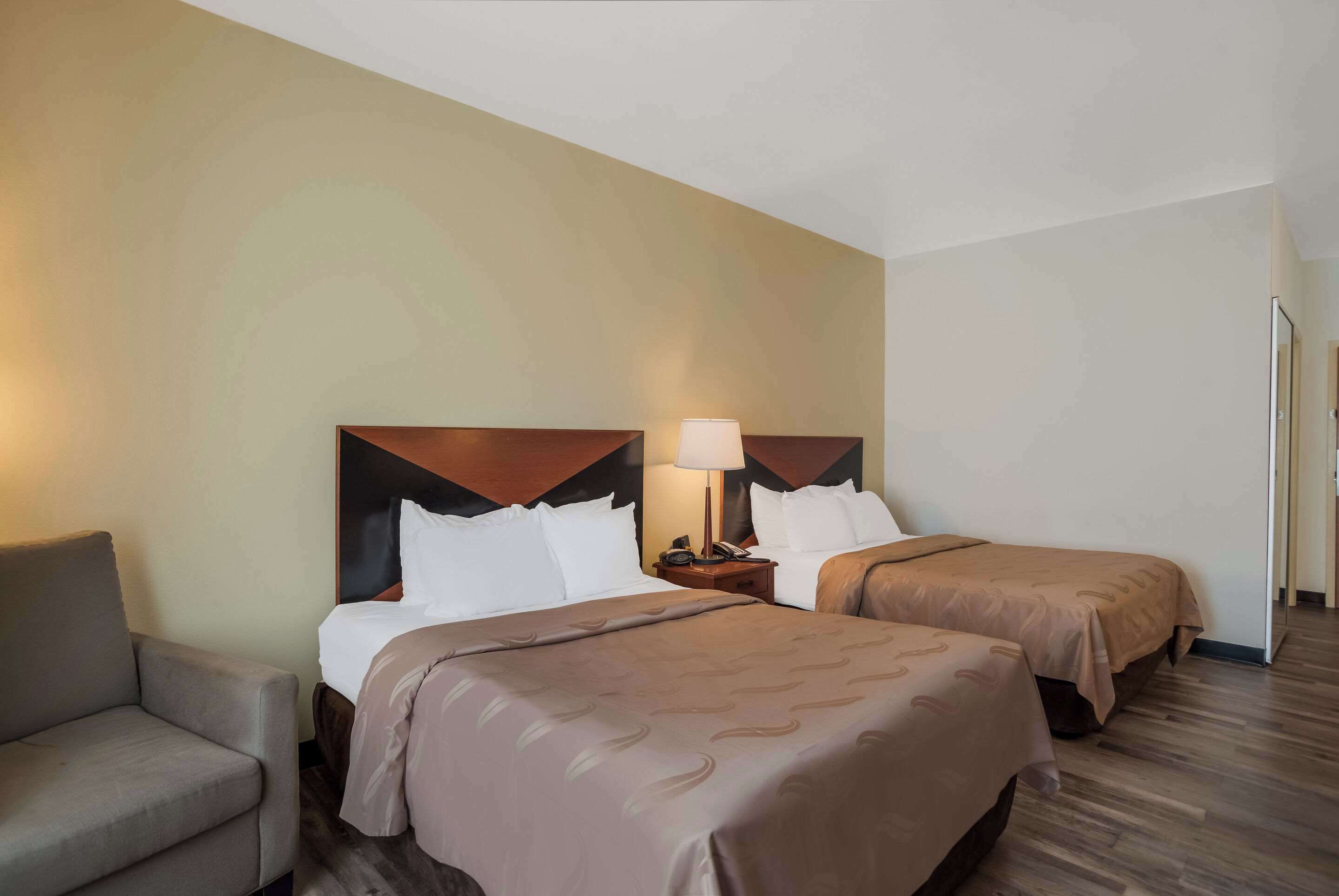 A hotel room with two beds, a sofa, and a nightstand with a lamp.