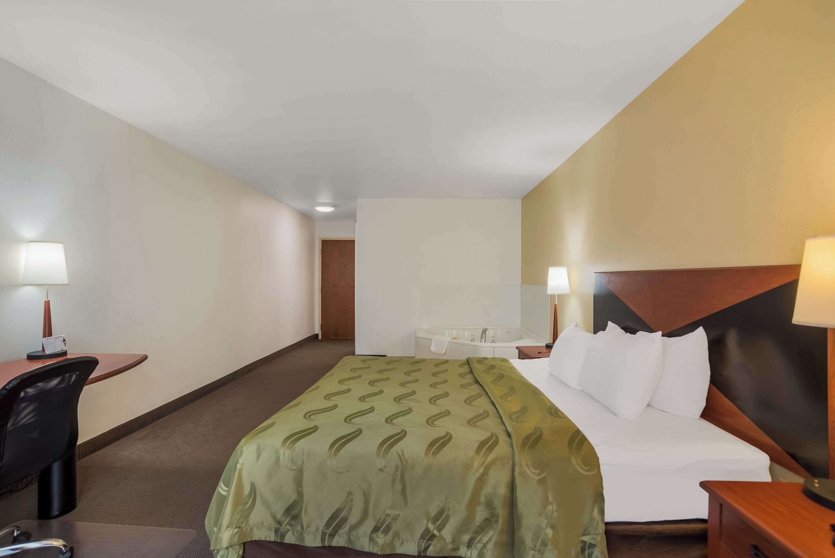 A hotel room with a bed, a desk, a chair, a bedside table, and a bathroom.