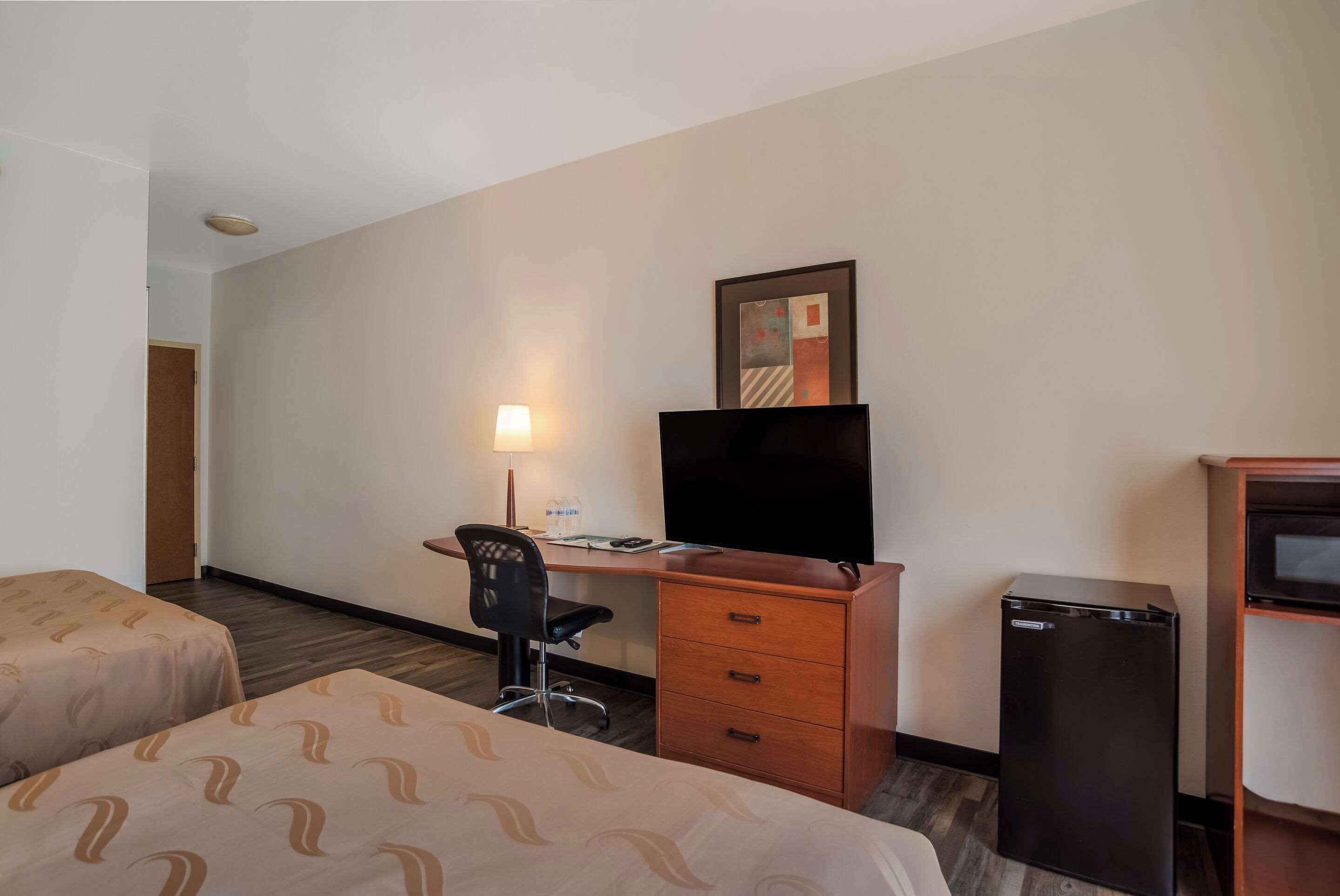 Une chambre d’hôtel avec deux lits, un bureau équipé d’un ordinateur et d’une lampe, une télévision et un petit réfrigérateur.