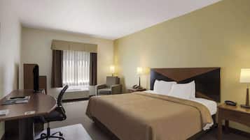 A hotel room with a large bed, a desk, a chair, a desk lamp, a bedside table, and a window with curtains.