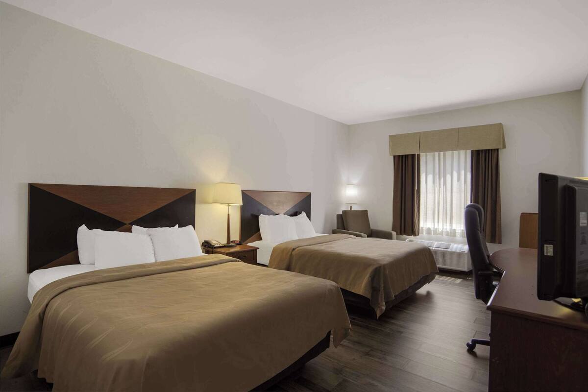 A hotel room with two beds, a desk, a chair, a television, and a window with curtains.