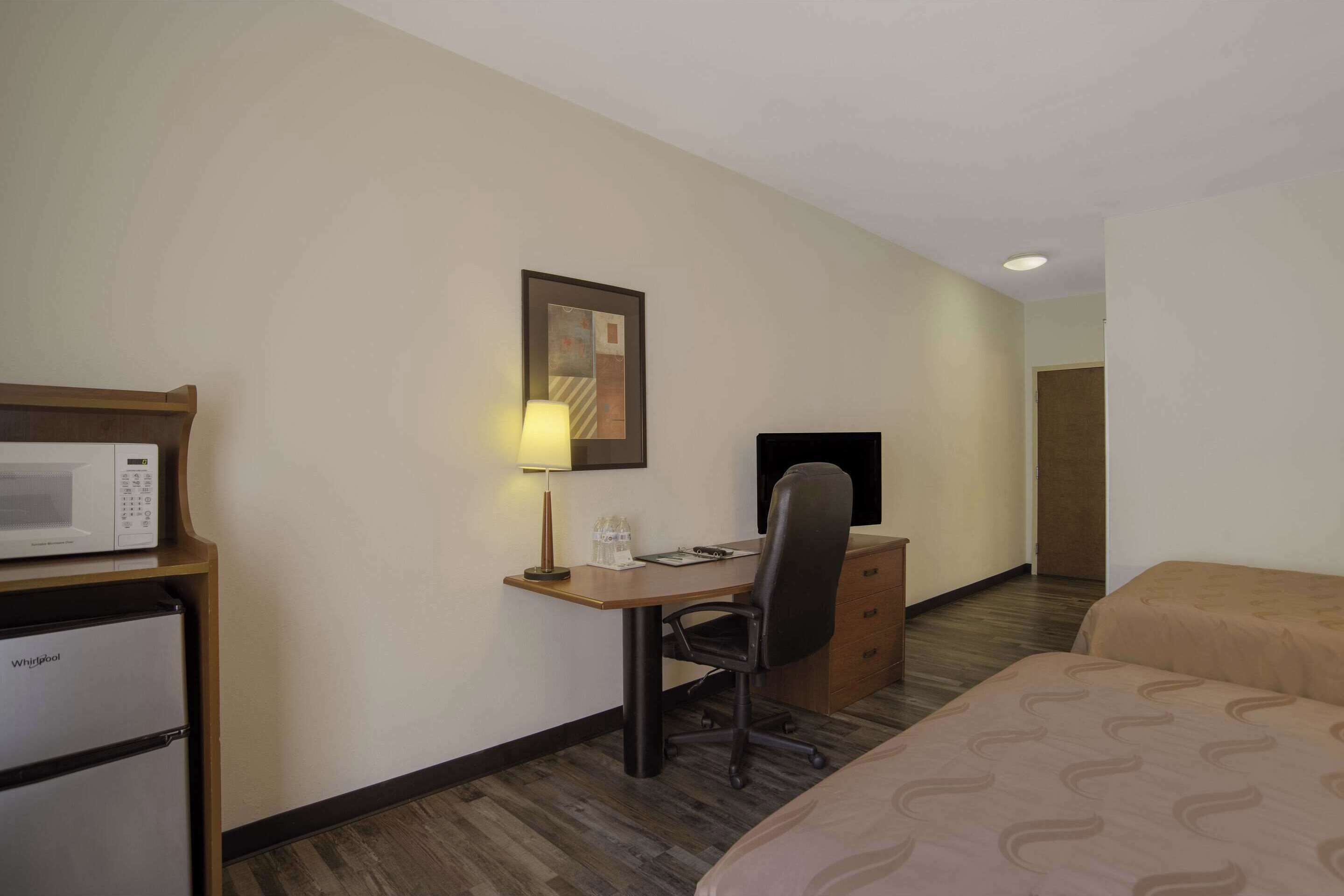 Una habitación de hotel con cama, escritorio con computadora, microondas y refrigerador.