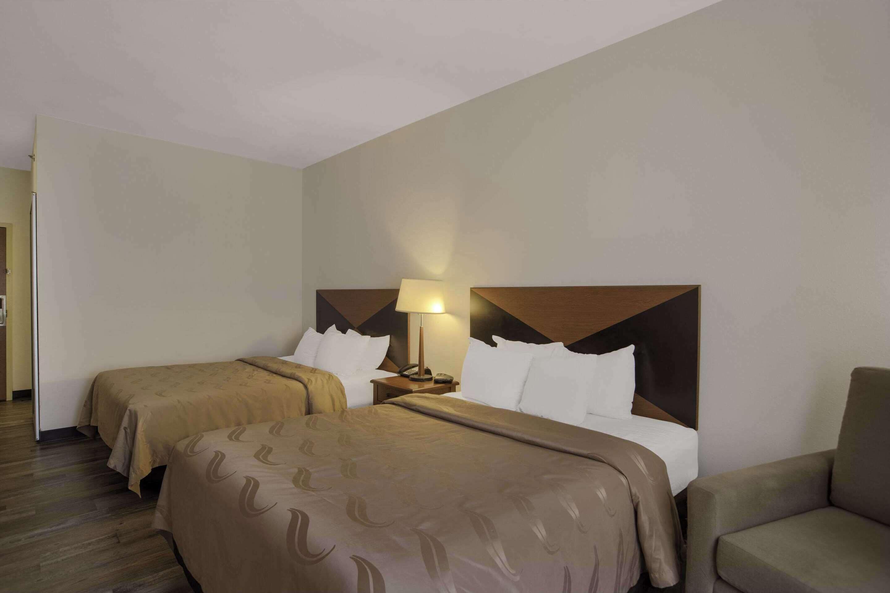 Une chambre d’hôtel avec deux lits, une table de chevet avec une lampe et une chaise.