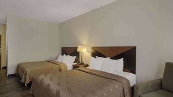 A hotel room with two beds, a nightstand with a lamp, and a chair.