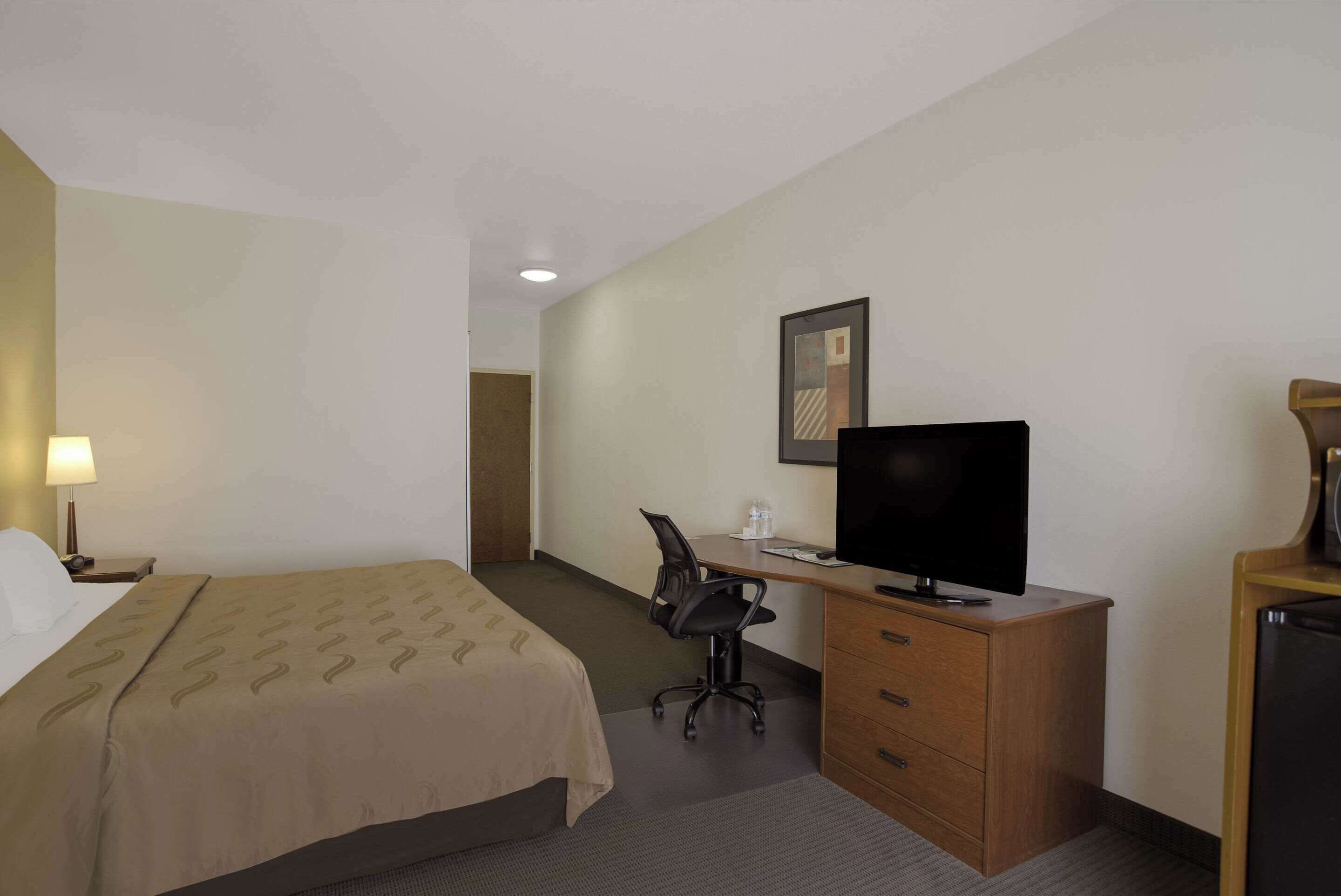 Una habitación de hotel con cama, escritorio, silla, televisor y cómoda.