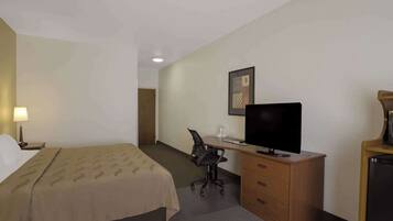 Una habitación de hotel con cama, escritorio, silla, televisor y cómoda.