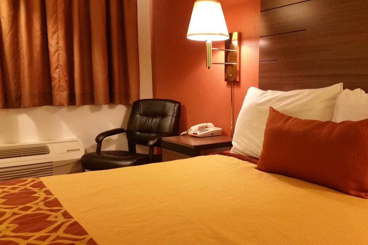 Una camera d'albergo con un letto, una sedia, un comodino con il telefono e una lampada.