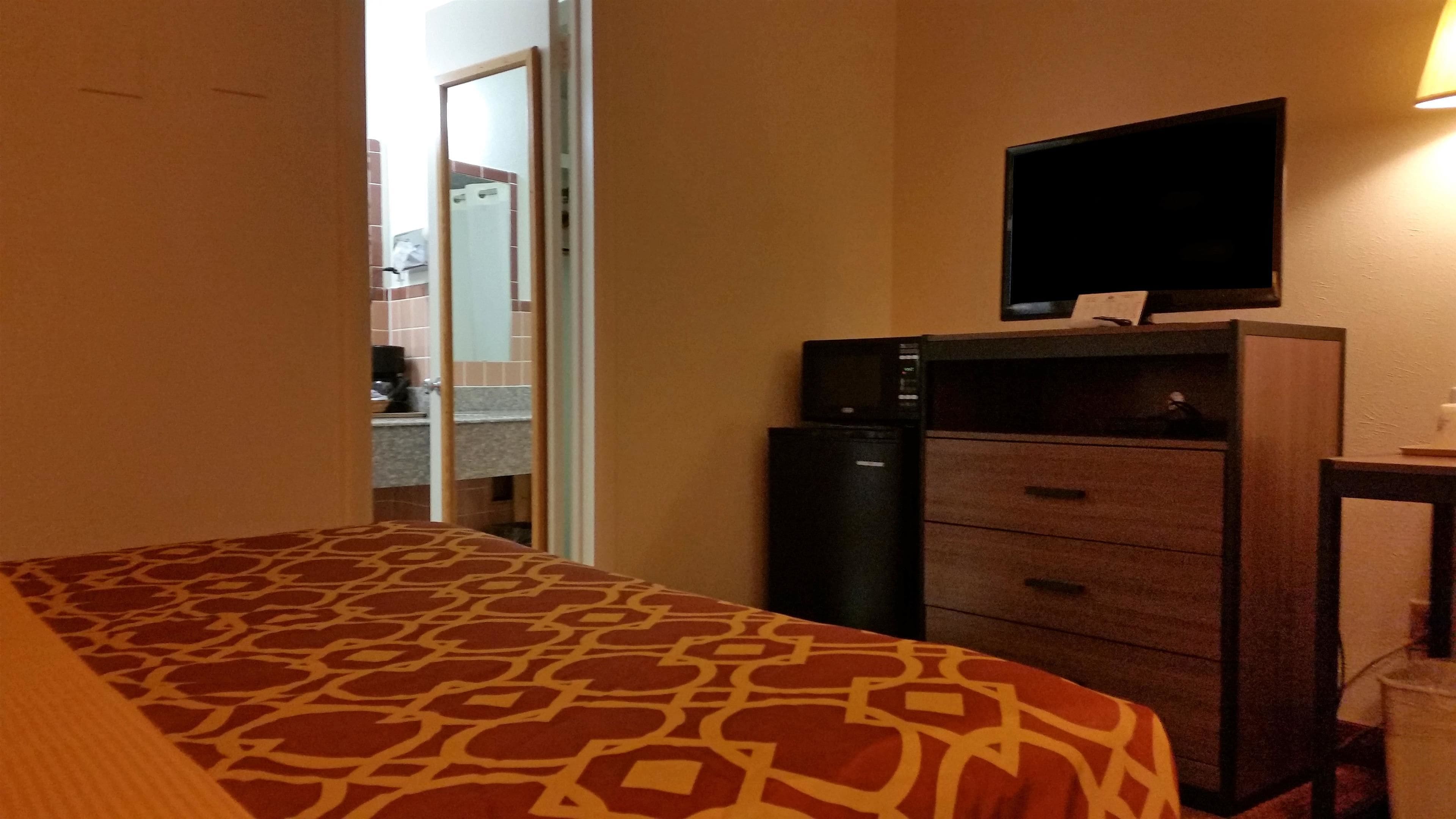 A hotel room with a bed, a desk with a computer, a television, and a minibar.