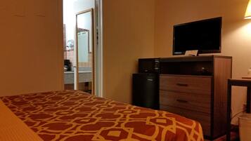 A hotel room with a bed, a desk with a computer, a television, and a minibar.
