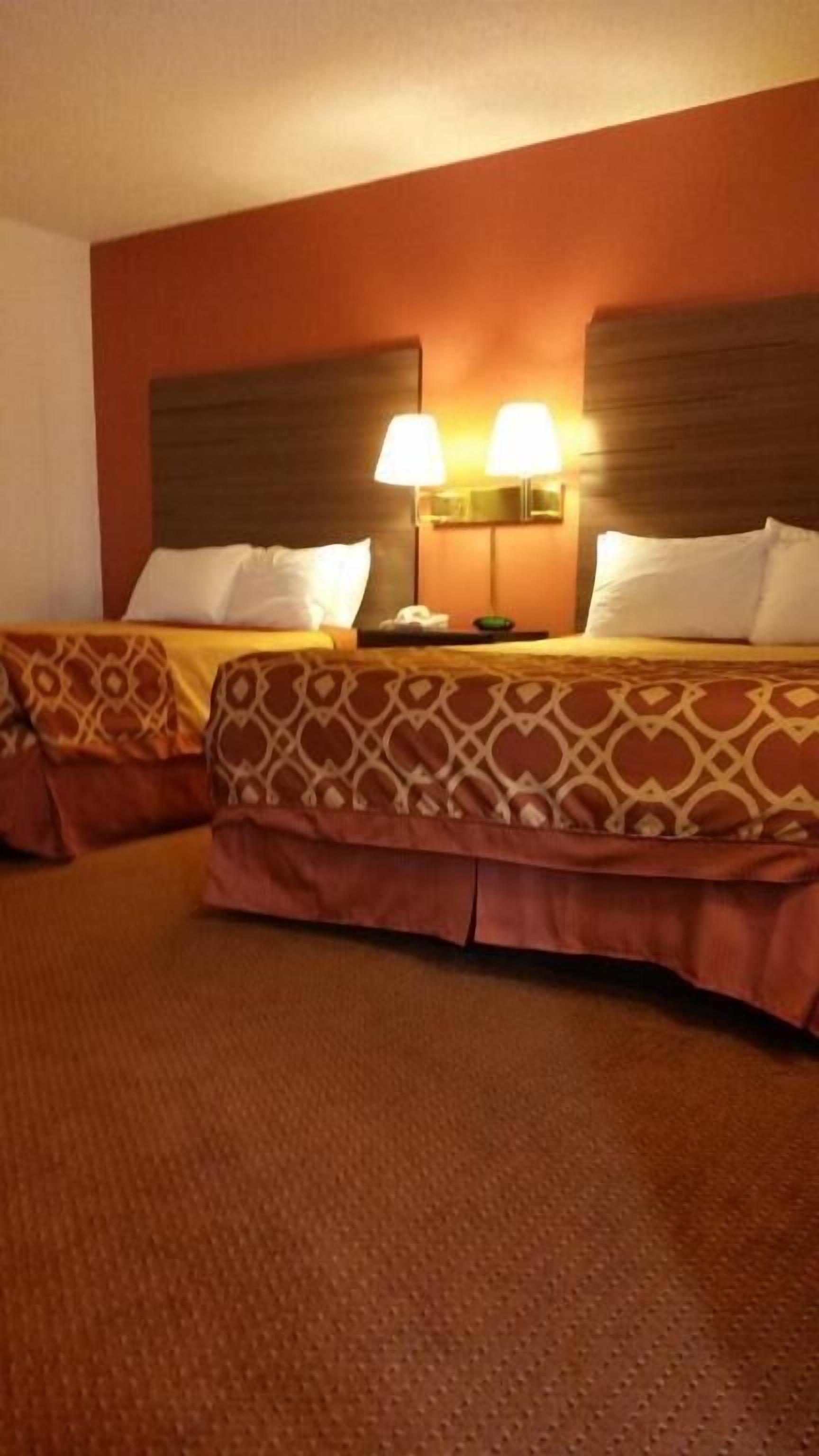 A hotel room with two beds, each with patterned bedding and headboards. There are two wall-mounted lamps on the headboard of the bed on the right.