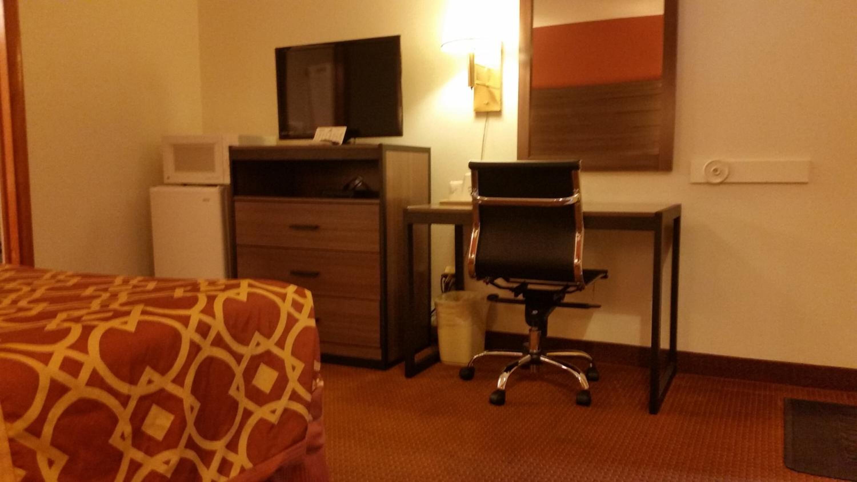 A hotel room with a bed, a desk with a chair, a television, and a small refrigerator.