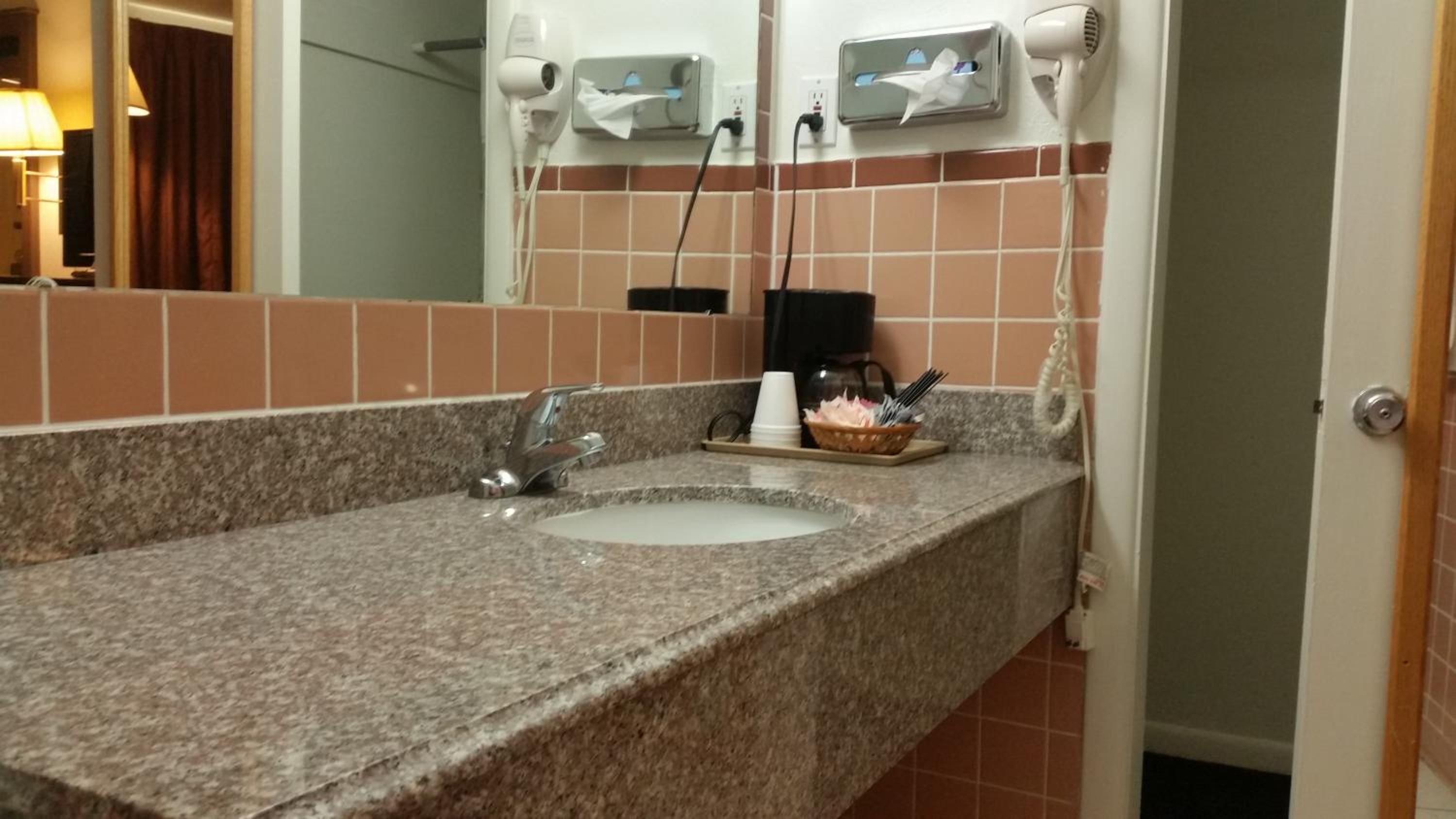 A bathroom with a granite countertop, two sinks, a hairdryer, and a telephone.
