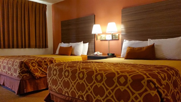 A hotel room with two beds, each with patterned bedding, a nightstand with a lamp, and a phone. - American Inn of Liberal (Liberal)