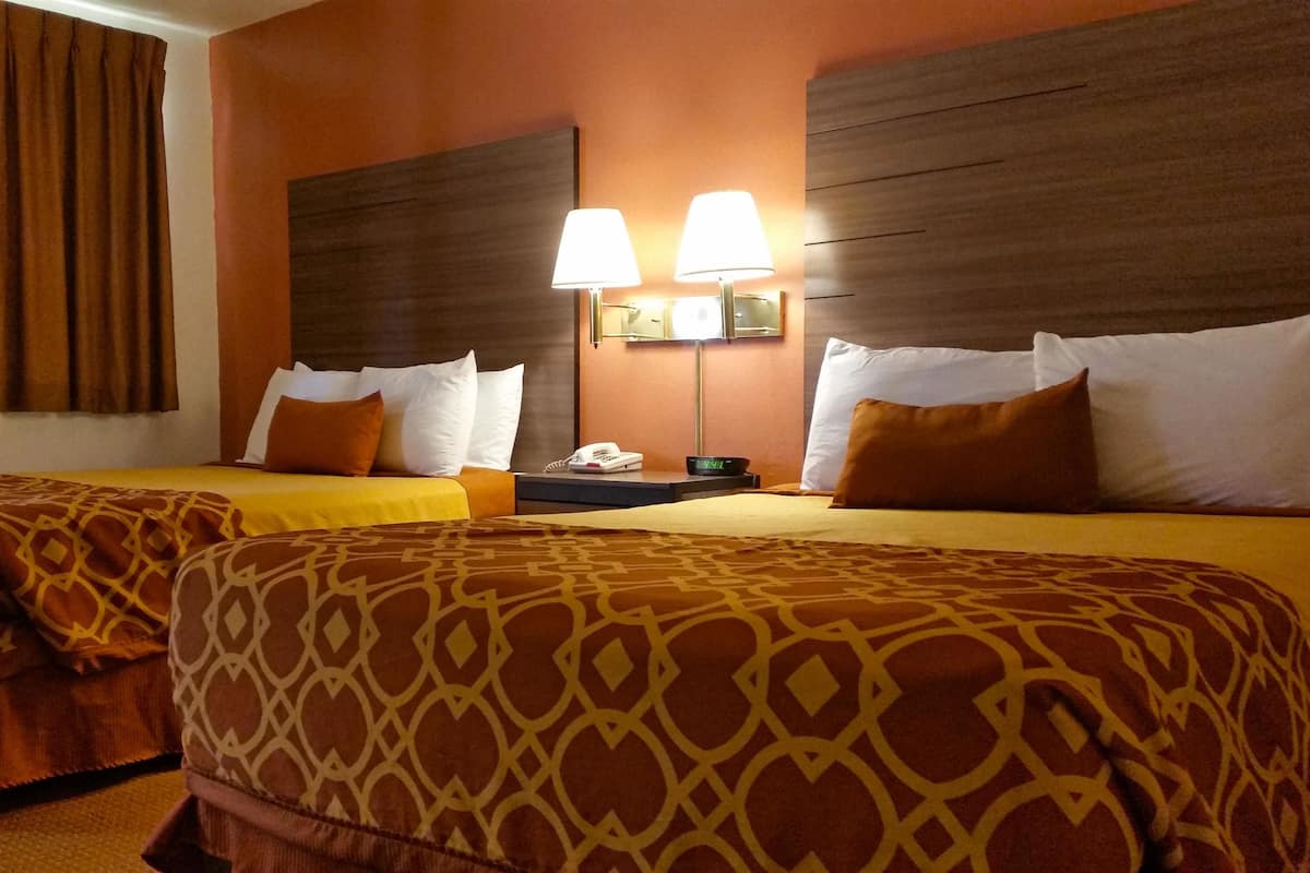 Una camera d'albergo con due letti, ognuno con biancheria a motivi decorativi, un comodino con lampada e telefono.
