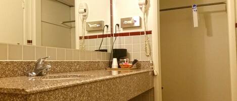 A bathroom with a granite countertop, a sink, a mirror, and two hair dryers mounted on the wall.
