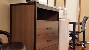 A hotel room with a wooden dresser, a flat-screen TV, a desk with a chair, and a refrigerator. - American Inn of Liberal (Liberal)