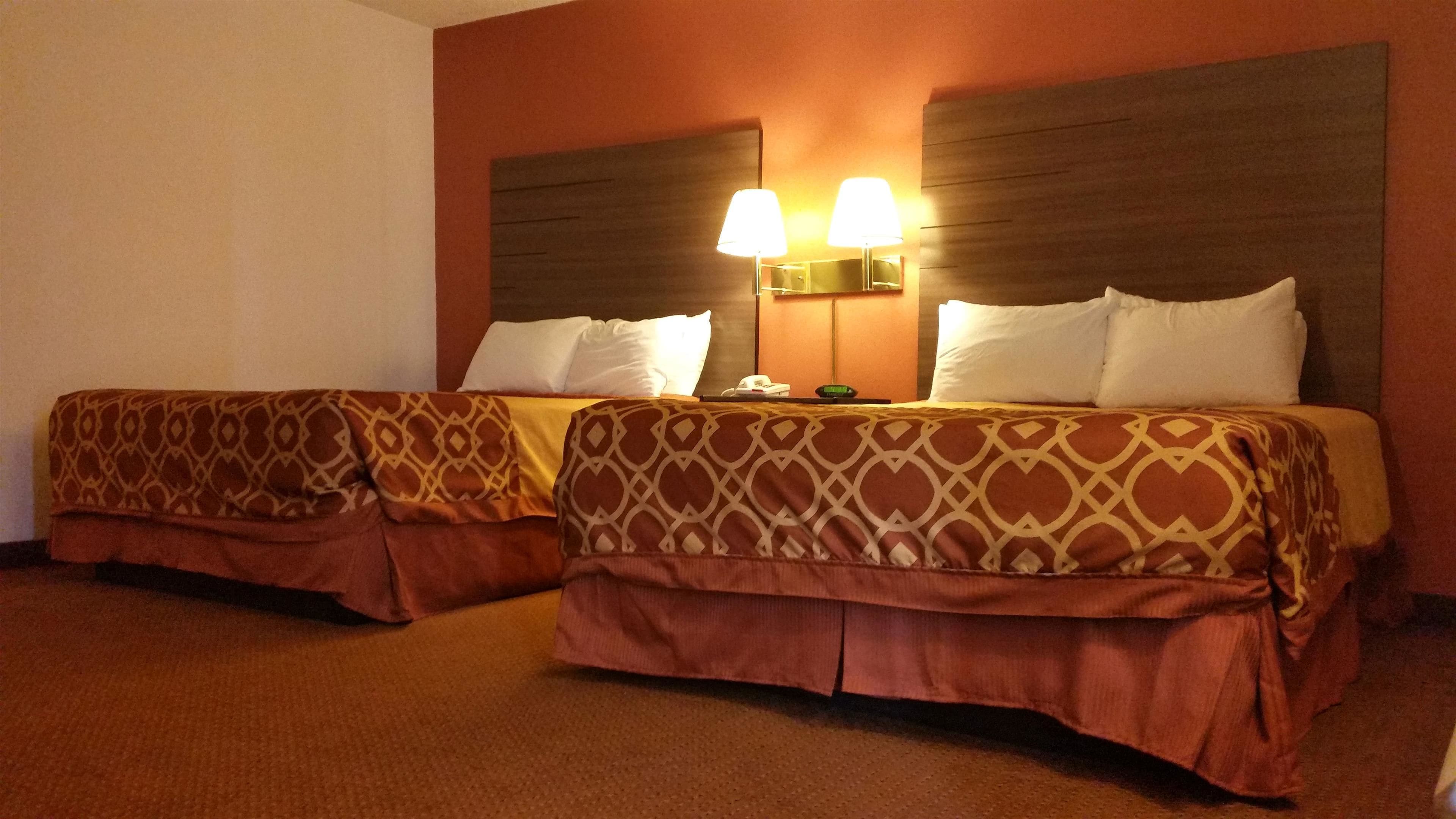 Habitación de hotel con dos camas, cada una con ropa de cama estampada y cabecero. Dos lámparas de pared están montadas en el cabecero.