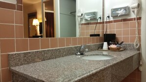 A bathroom with a granite countertop, a sink, a mirror, and a hairdryer mounted on the wall. - American Inn of Liberal (Liberal)
