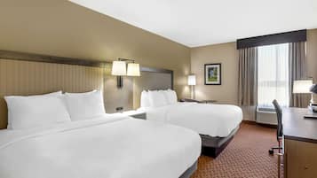 Ein Hotelzimmer mit zwei Betten, einem Schreibtisch und einem Sessel. Es gibt ein Fenster mit Vorhängen, eine Wandlampe und ein gerahmtes Bild.