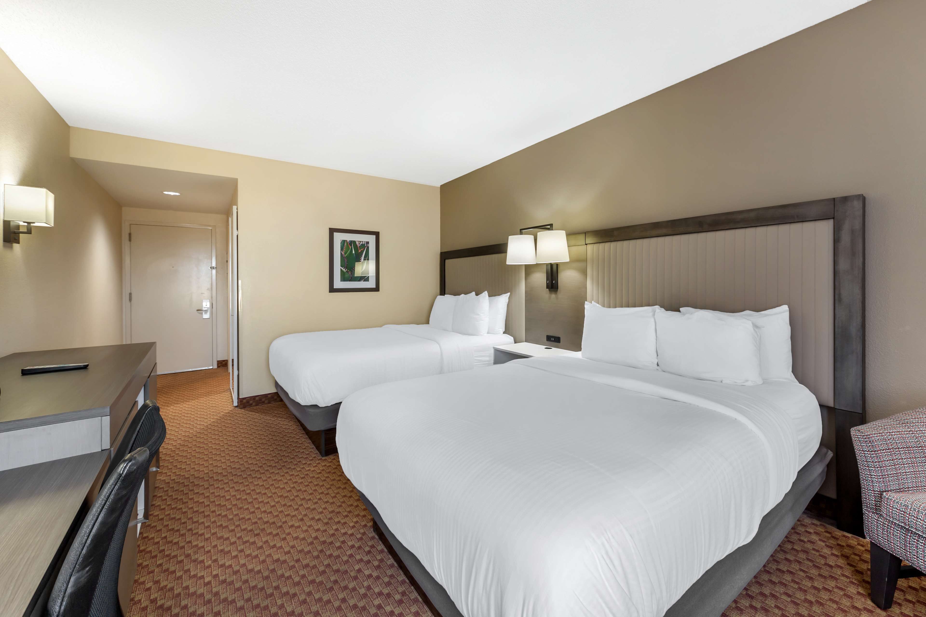 A hotel room with two beds, a desk, and a chair.