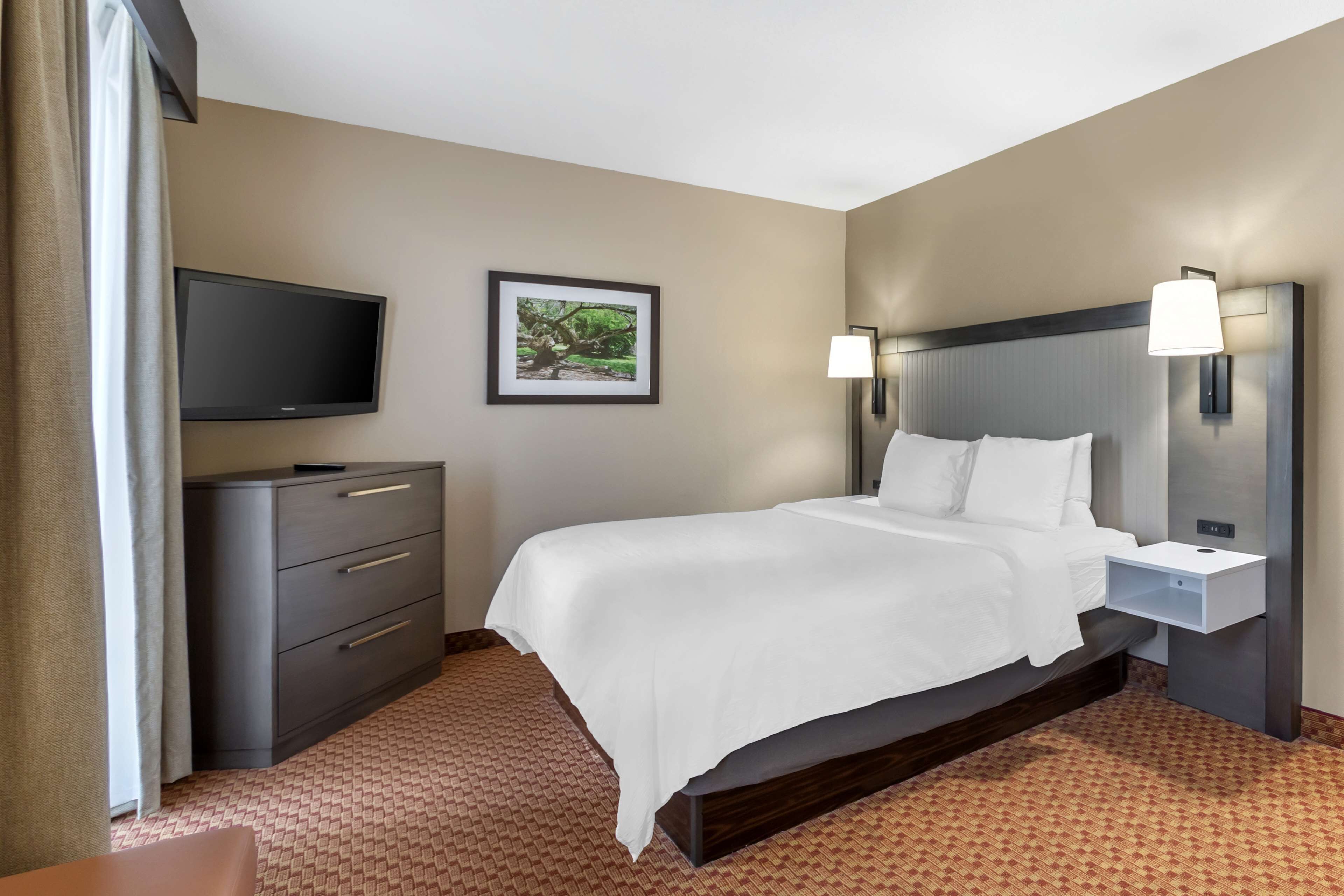A hotel room with a bed, a TV, a desk, and a lamp.