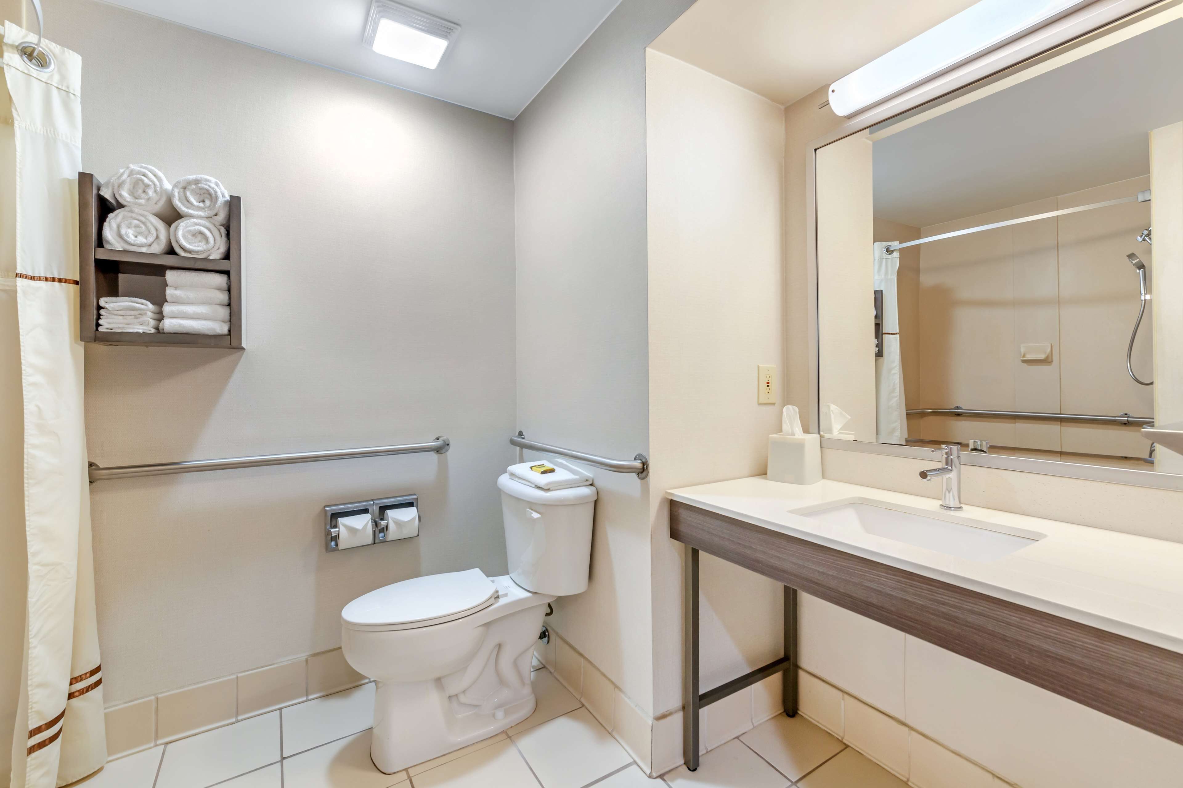A modern bathroom with a toilet, sink, and shower. There are towels on a shelf and a mirror above the sink.