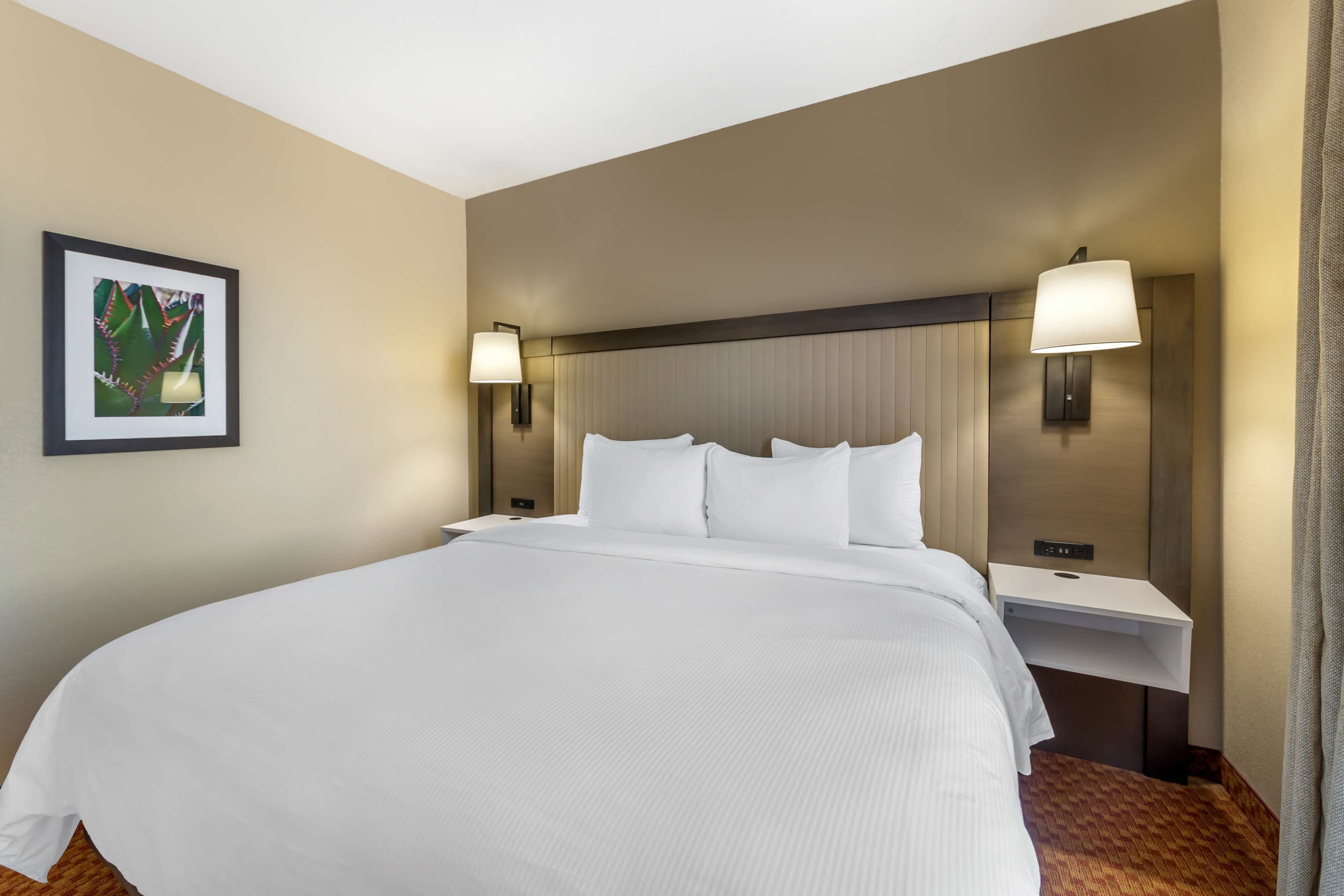 A hotel room with a large bed, two bedside tables, a headboard, and a wall-mounted lamp.