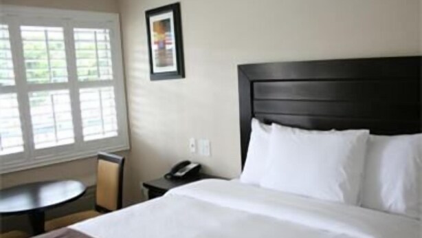 A hotel room with a large bed, a bedside table with a phone, a small round table, and a window with blinds.
