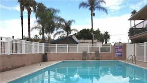 A swimming pool with a white fence, palm trees, and a building in the background.