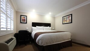 A hotel room with a bed, bedside table, chair, and artwork on the walls.