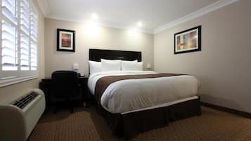 A hotel room with a bed, bedside table, chair, and artwork on the walls.