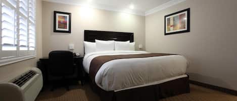 A hotel room with a bed, bedside table, chair, and artwork on the walls.