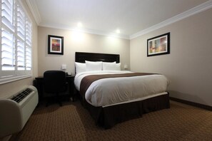 A hotel room with a bed, bedside table, chair, and artwork on the walls.