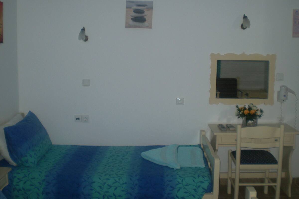 Un dormitorio con una cama, un escritorio con silla, un espejo y una lámpara fijada a la pared.