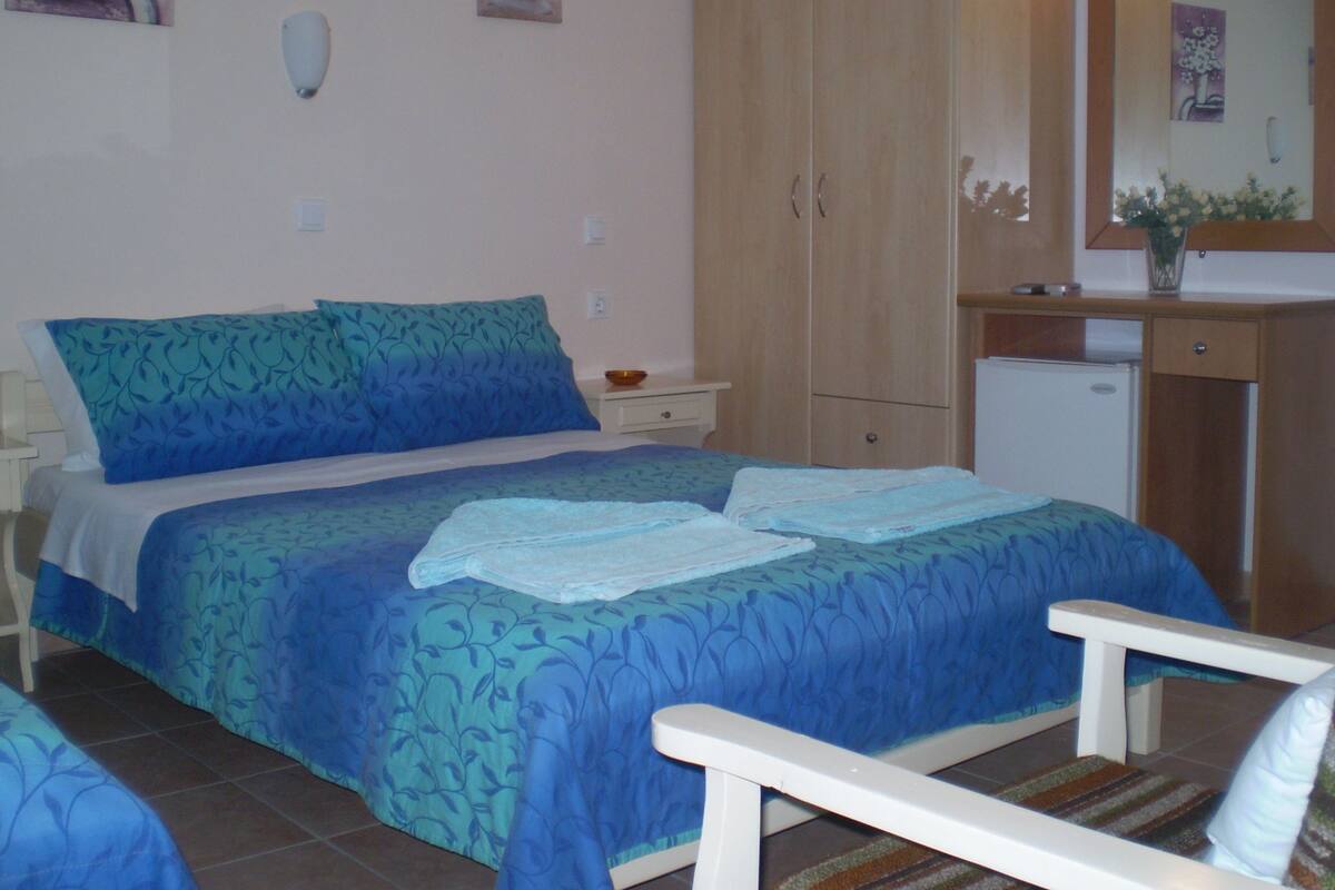 Un dormitorio con cama, mesita de noche, cómoda, espejo y un pequeño escritorio con un florero.