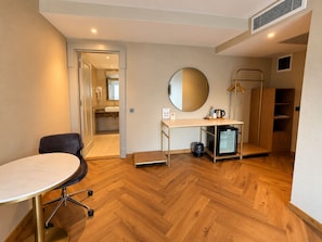 A hotel room with a wooden floor, a round mirror, a small refrigerator, a desk, a chair, and a wardrobe. - Faros Hotel Old City - Special Class (Istanbul)