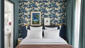 A hotel room with a bed, a nightstand, a framed picture, and a bathroom visible through an open door.