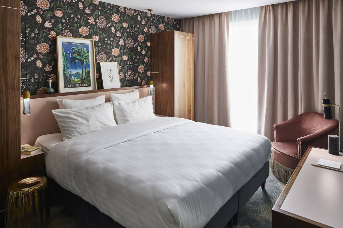 Une chambre d’hôtel avec un grand lit, une armoire en bois, un bureau avec une lampe et une chaise.