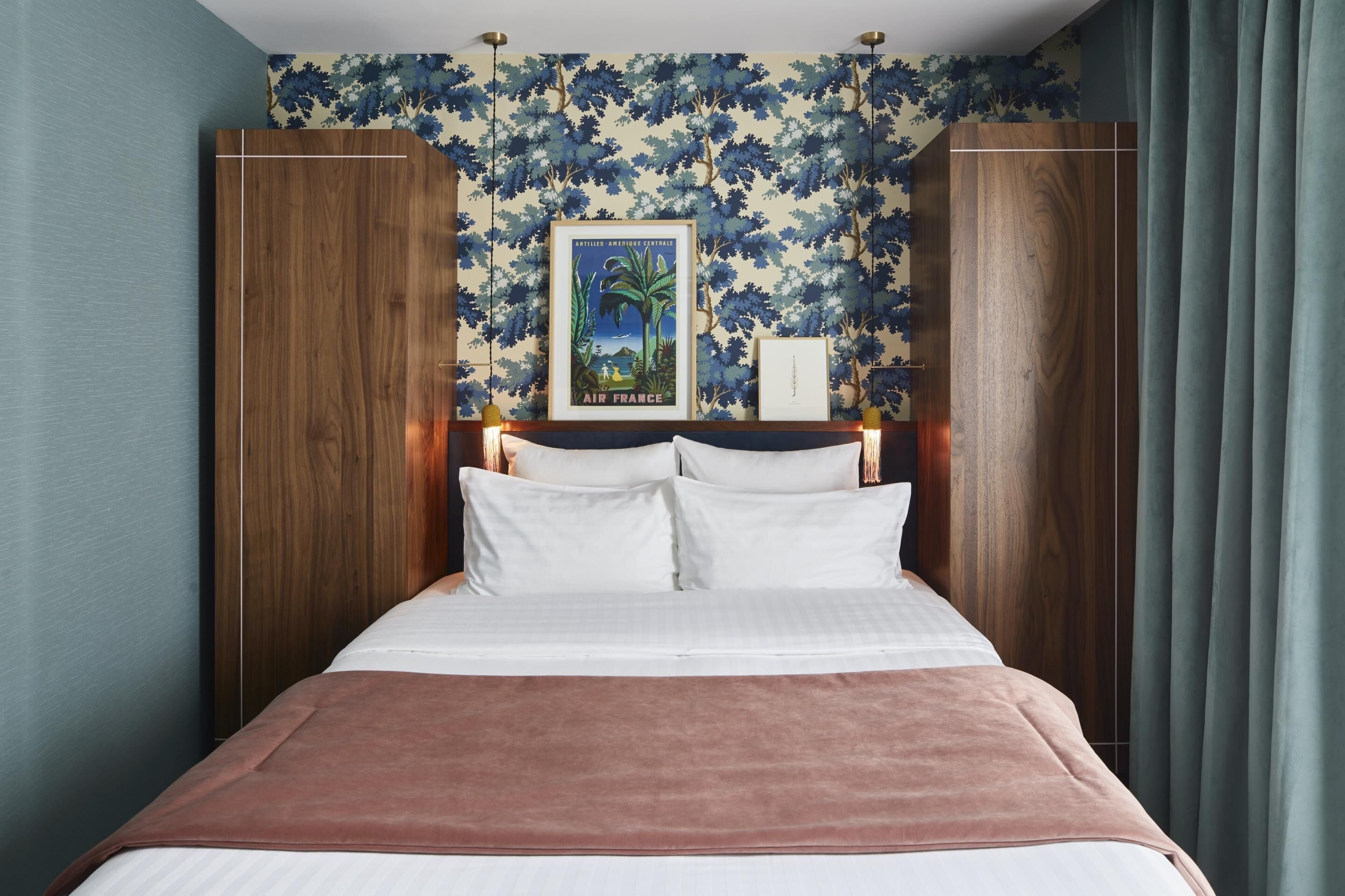 Una cama bien hecha con ropa de cama blanca y rosa, un cuadro enmarcado encima y papel tapiz floral azul.