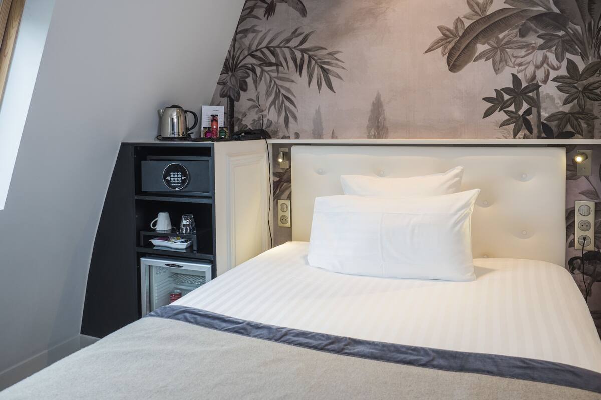 Une chambre d’hôtel équipée d’un lit, d’un mini-bar, d’une machine à café et d’un mur orné d’un motif floral.