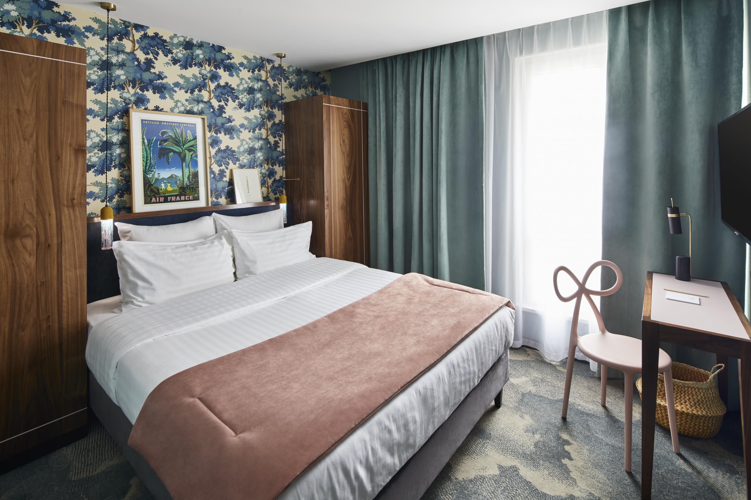 A hotel room with a large bed, a desk, a chair, a TV, and a framed picture on the wall.