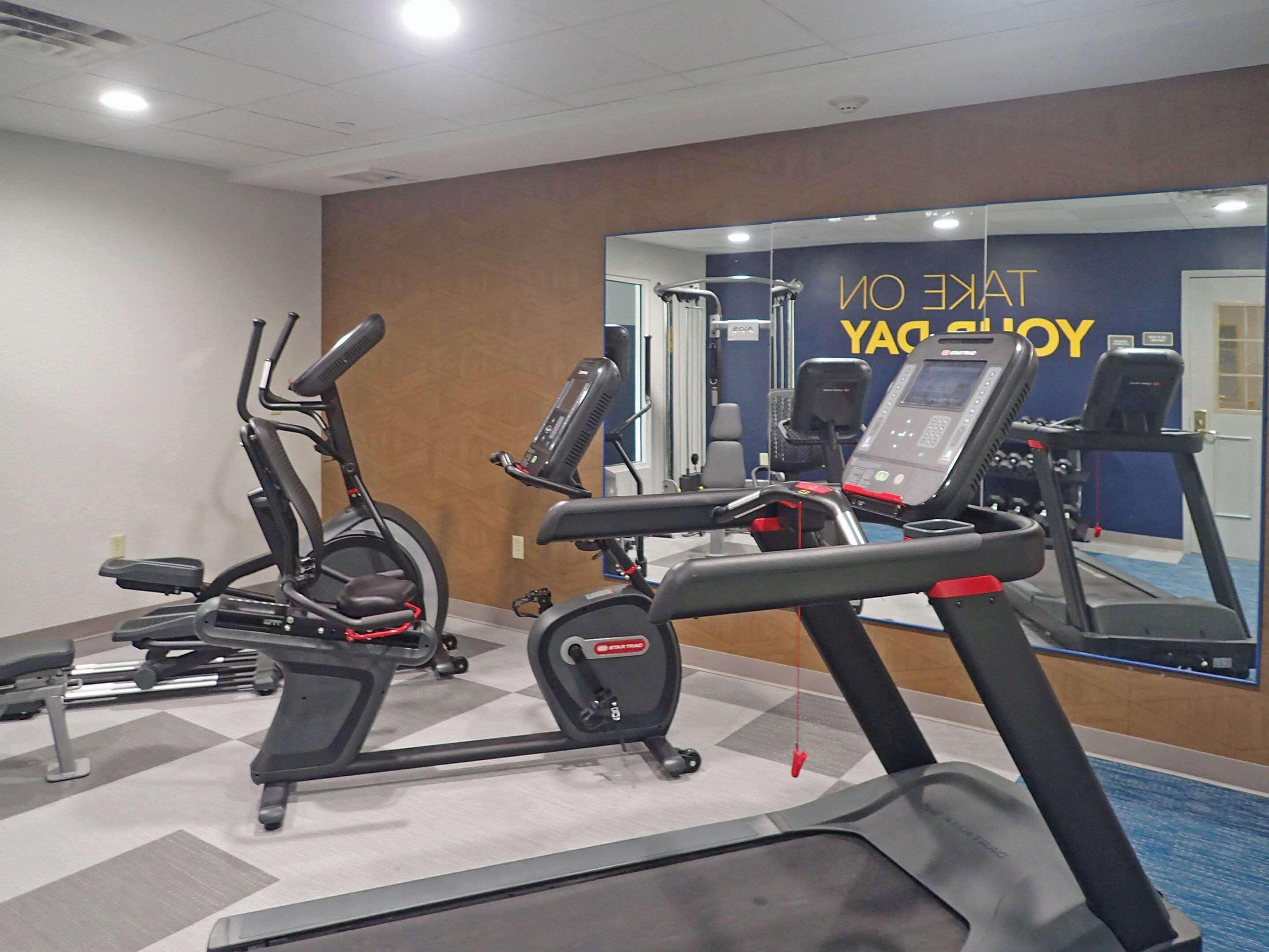 Un gimnasio con varios equipos de ejercicio, incluyendo cintas de correr y elípticas.