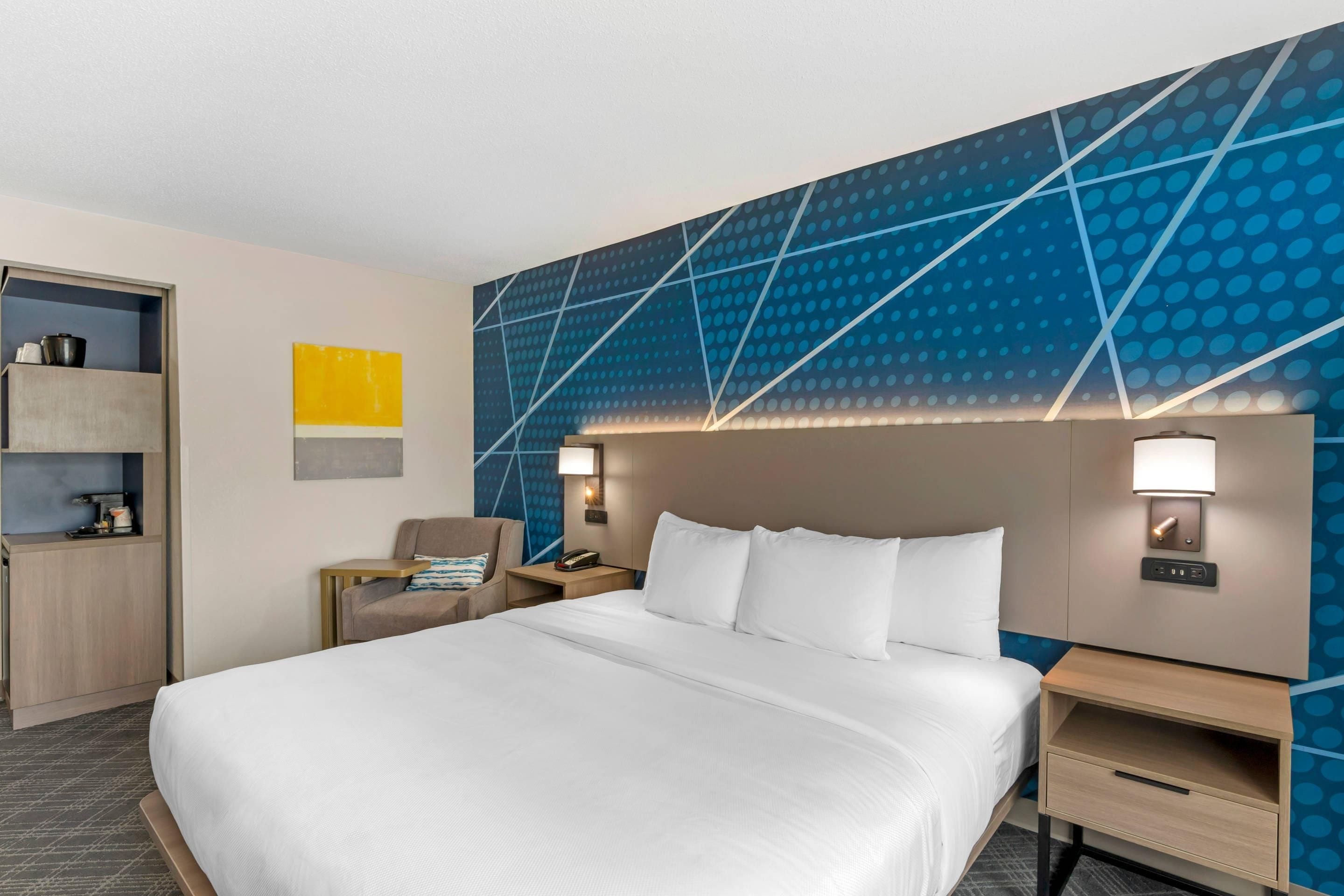 Una habitación de hotel con una cama grande, una mesita de noche, una silla y una pared con un diseño geométrico.
