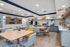 A modern restaurant with a central counter, seating area, and kitchen in the background. - Comfort Inn & Suites Hampton near Coliseum (Hampton)