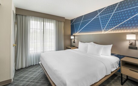 A hotel room with a large bed, a nightstand, a wall-mounted lamp, and a window with curtains.