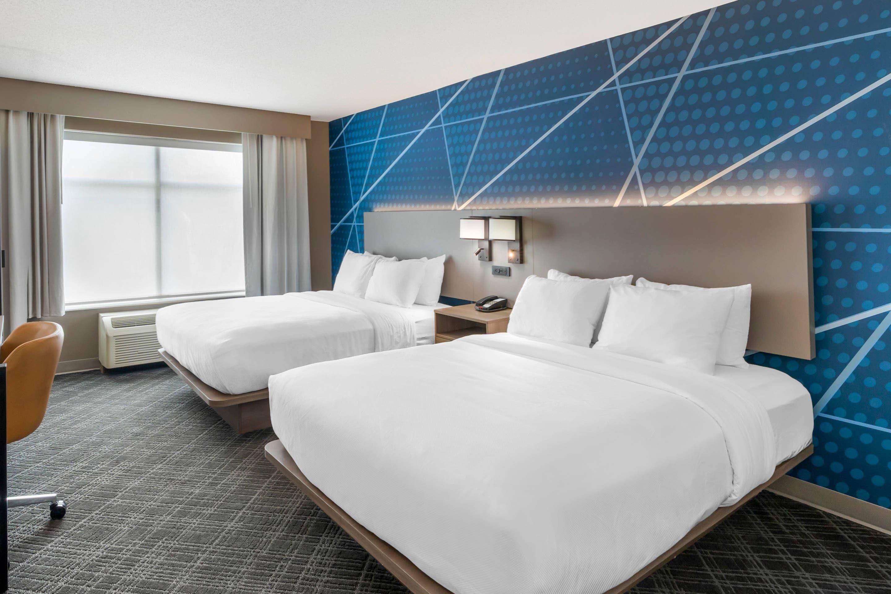 A hotel room with two beds, a desk, a chair, and a large window.